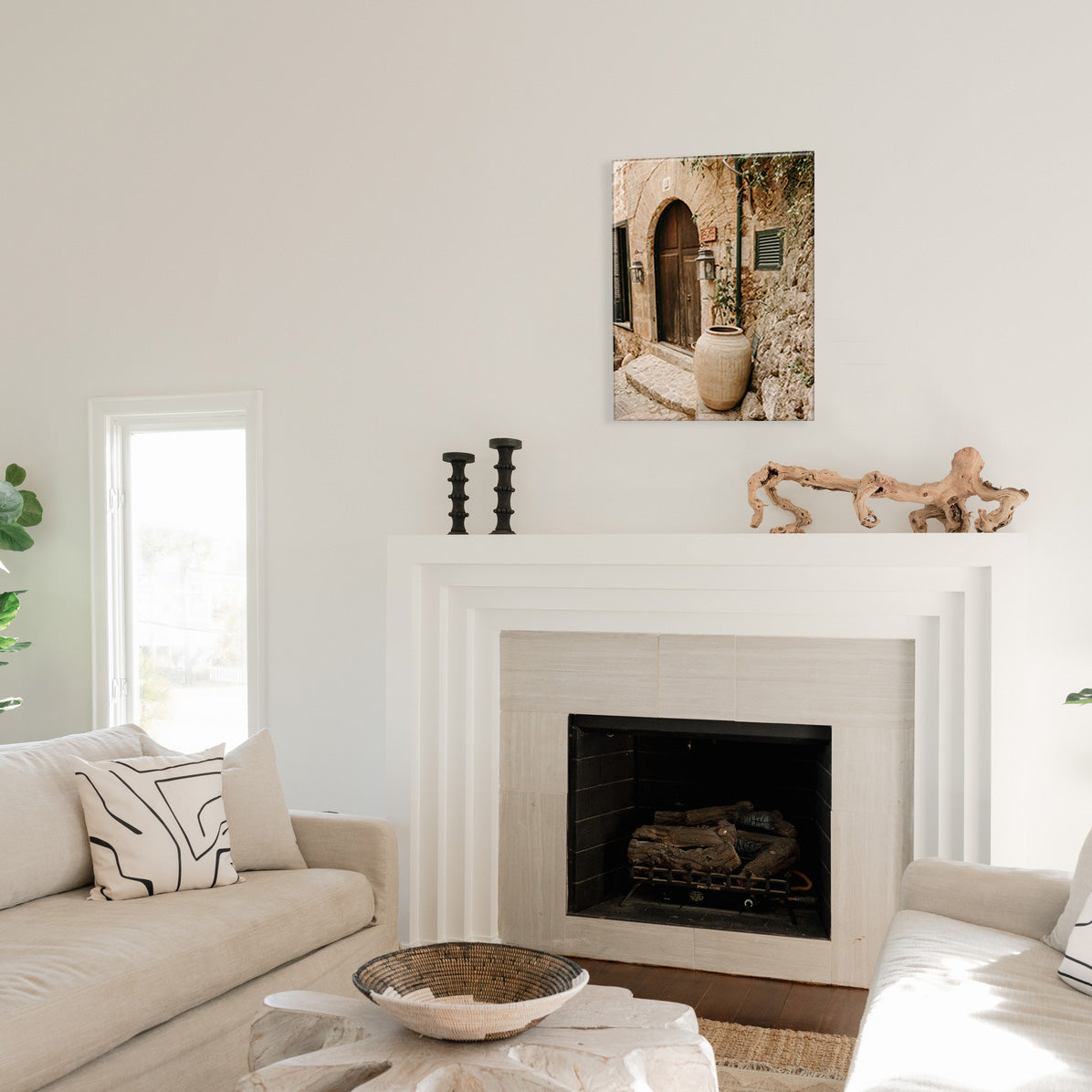 Living room with a fireplace, decorative items, and a glass print of an arched doorway and large flower pot.