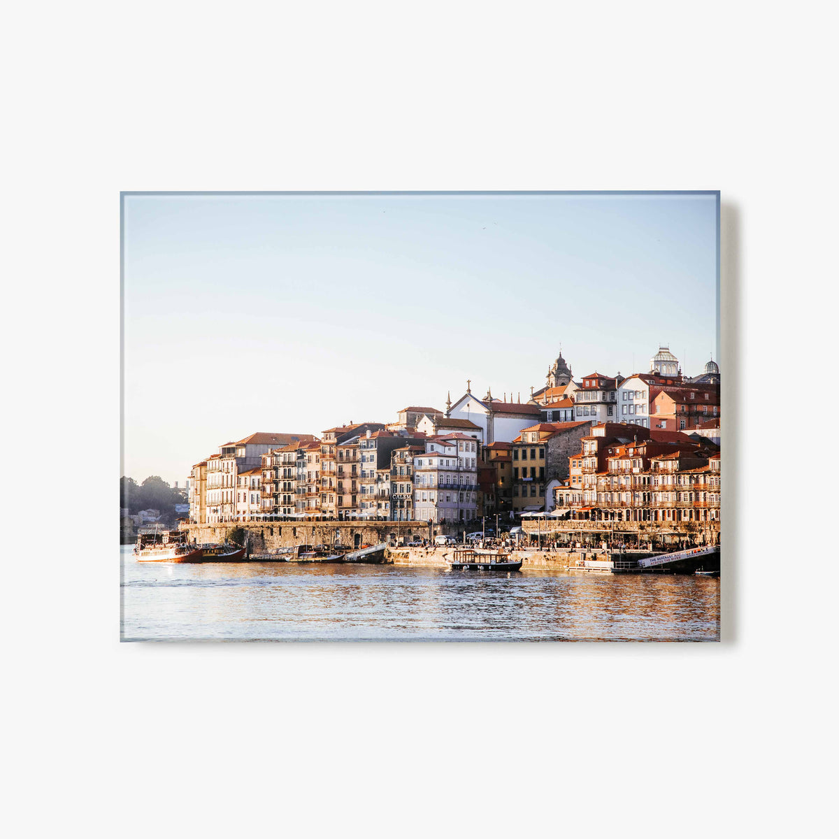 Glass print of a the Porto riverside with buildings along a waterfront and a golden glow from the sun.