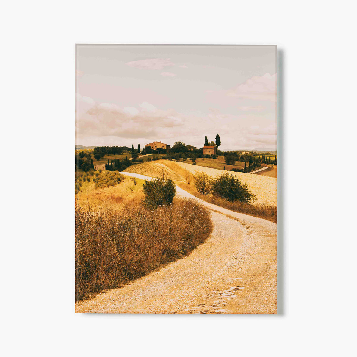Glass print of winding road through a scenic landscape with rolling hills and buildings.